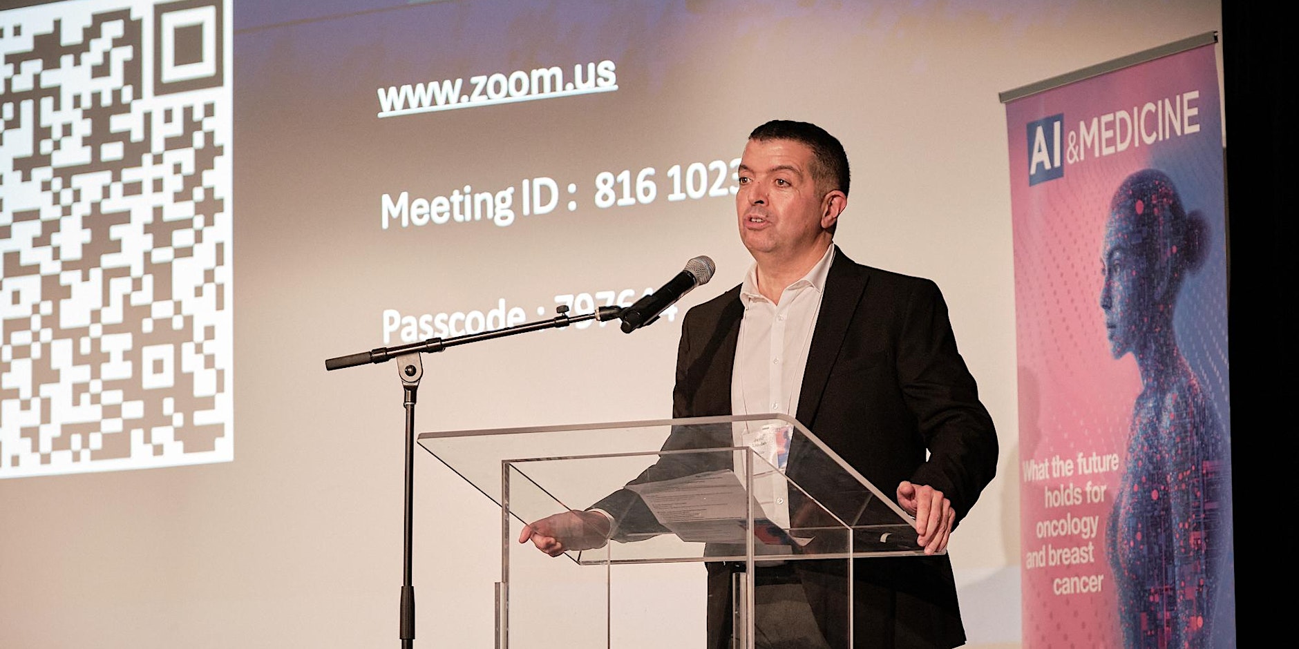 A speaker on stage at the previous Montreal Summit on AI and Oncology, beside a banner reading AI and Medicine, what the future holds for oncology and breast cancer
